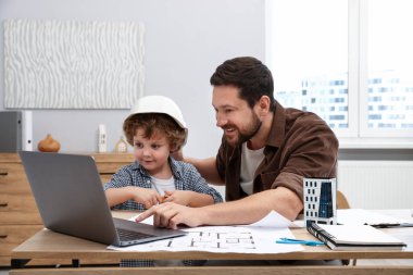 Meslek seçimi. Babası ve oğlu evde dizüstü bilgisayar ve mühendislik çizimleri ile masada.