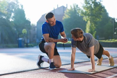 Genç adam profesyonel antrenörle dışarıda egzersiz yapıyor.