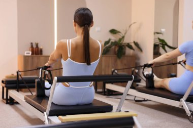 Stüdyoda reformcular üzerinde egzersiz yapan kadın ve pilates eğitmeni.