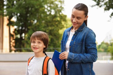 Anne, oğlunu okula götürürken sırt çantasına kitap koydu.