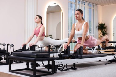 Stüdyoda reformcular üzerinde egzersiz yapan kadın ve pilates eğitmeni.