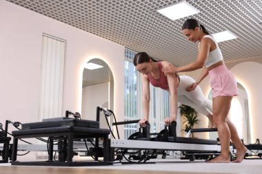 Stüdyoda pilates eğitmeninin gözetiminde reformcu bir kadın. Düşük açı.