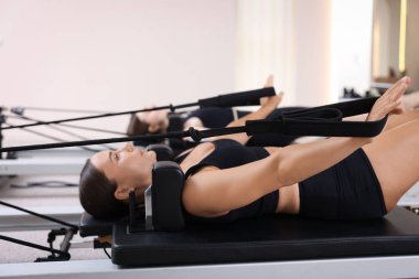 Stüdyoda reformcular üzerinde egzersiz yapan kadın ve pilates eğitmeni, seçici odaklanma