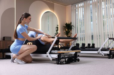 Stüdyoda pilates eğitmeni tarafından yönetilen reformcu kadın üzerinde egzersiz yapıyor.