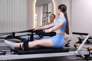 Stüdyoda reformcular üzerinde egzersiz yapan kadın ve pilates eğitmeni.