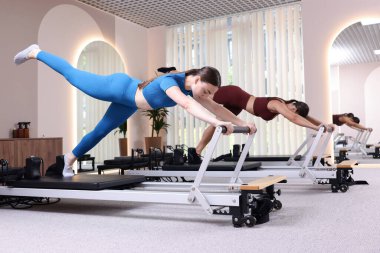 Stüdyoda reformcular üzerinde egzersiz yapan kadın ve pilates eğitmeni.