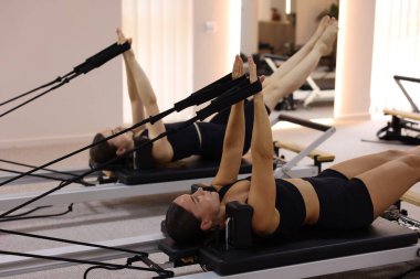Stüdyoda reformcular üzerinde egzersiz yapan kadın ve pilates eğitmeni.
