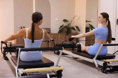 Stüdyoda reformcular üzerinde egzersiz yapan kadın ve pilates eğitmeni.
