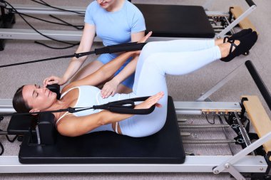 Stüdyoda pilates eğitmeni tarafından yönetilen reformcu kadın üzerinde egzersiz yapıyor.