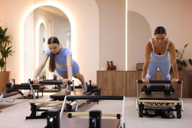 Stüdyoda reformcular üzerinde egzersiz yapan kadın ve pilates eğitmeni.