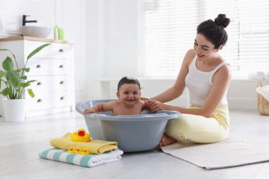 Anne küçük bebeğini evde yıkıyor.