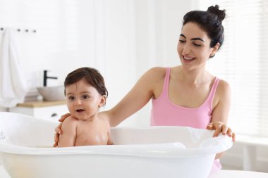 Anne küçük bebeğini evde yıkıyor.