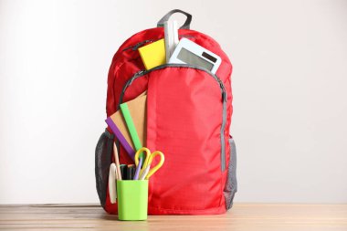 Kırmızı sırt çantası ve ahşap masa üzerindeki farklı kırtasiye malzemesi.