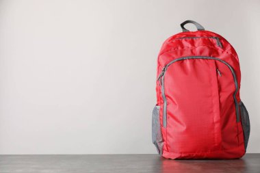 Gri masadaki kırmızı sırt çantası ışık arkaplanı, metin için boşluk