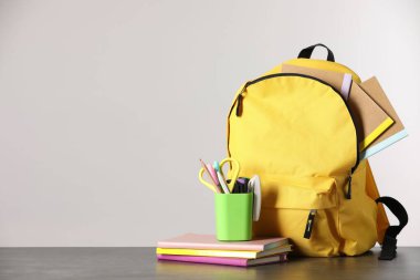 Masanın üzerinde farklı kırtasiye malzemesi olan sarı sırt çantası. Metin için boşluk