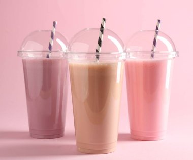 Pembe arka planda plastik bardaklarda lezzetli milkshake.