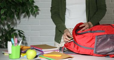 Masadaki kırmızı çantaya farklı kırtasiye malzemesi koyan kadın, yakın plan.