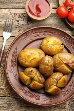 Lezzetli fırında patatesler, çatal, baharatlar ve domatesler ahşap masada, düz uzanmış.