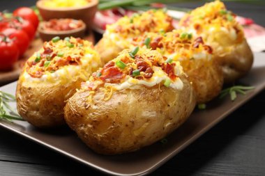 Siyah ahşap masada lezzetli fırınlanmış patatesler, yakın plan.