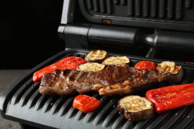 Gri masada biftekli ve sebzeli elektrikli ızgara, yakın plan.