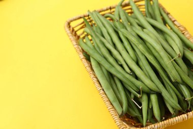 Sarı arka planda sepette taze yeşil fasulye kabukları, yakın plan. Metin için boşluk