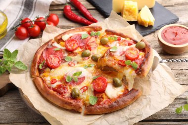 Taking piece of delicious pizza with cheese, tomatoes and olives at wooden table, closeup