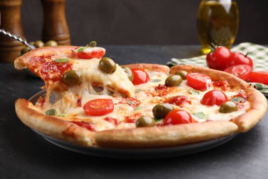 Peynirli, domatesli ve zeytinli lezzetli pizzayı koyu gri masada yakın plan çekiyoruz.