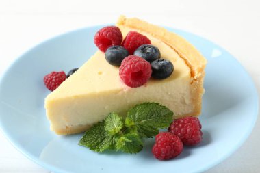 Piece of delicious cheesecake with fresh berries and mint on white table, closeup