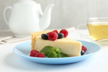 Beyaz masada servis edilen taze böğürtlenli ve nane şekerli nefis bir cheesecake.