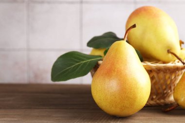 Yeşil yapraklı taze armutlar ve ahşap masadaki hasır sepet açık gri fayanslı duvara yakın çekim. Metin için boşluk