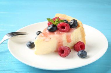 Açık mavi ahşap masada böğürtlenli ve soslu lezzetli bir cheesecake.