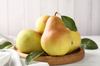 Taze armutlar ve yeşil yapraklar beyaz ahşap masada, yakın plan.