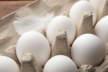 Yumurta kutusunda çiğ tavuk yumurtası ve tüy, yakın plan.