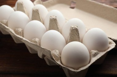 Yumurta kartonundaki çiğ tavuk yumurtaları ahşap masada, yakın plan.