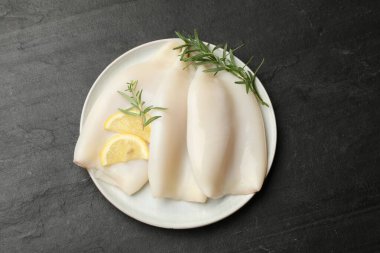 Uncooked squids with lemon slices and rosemary on black table, top view