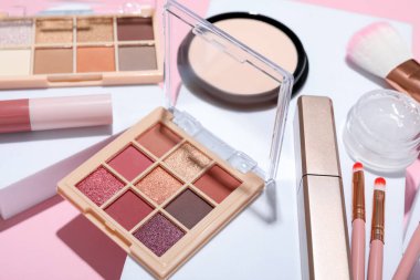 Renkli göz falı paletleri, diğer kozmetik ürünler, podyumlar ve pembe arka planda makyaj fırçaları, yakın plan