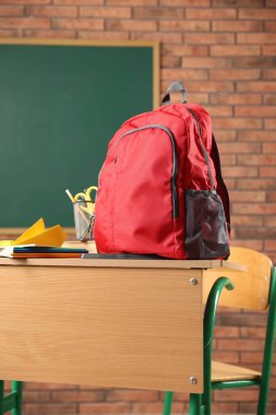 Kırmızı sırt çantası, farklı kırtasiye malzemesi ve sınıftaki masada kağıt uçak.