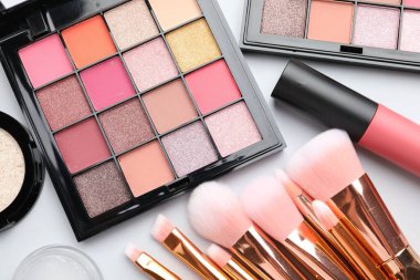 Eyeshadow palettes, other cosmetic products and brushes on white background, flat lay