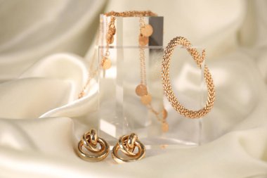 Hafif ipek kumaş üzerine altın mücevherlerin şık sunumu, yakın plan.