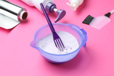 Care cosmetic product for blonde hair in bowl and hairdresser's tools on pink background, closeup
