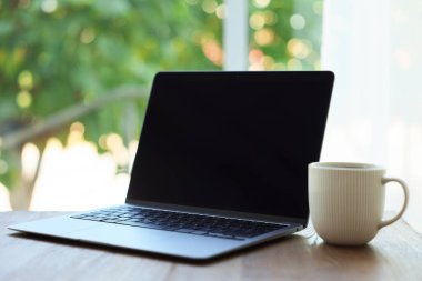 Laptop ve fincanı ahşap masada, bulanık yeşil arka planda, yakın plan. Tasarım için model