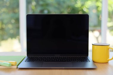 Laptop 'u, kırtasiyeyi ve kupayı açık bırak. Bulanık yeşil arka plan, yakın plan. Tasarım için model