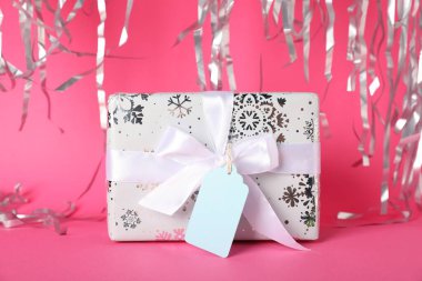 Boş etiketli hediye kutusu ve pembe arka planda flamalar, yakın plan.