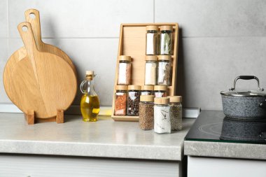 Cam kavanozlarda farklı baharatlar ve mutfakta açık gri masada yağlar.