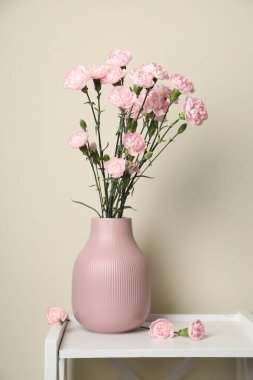 Beyaz vazodaki karanfil çiçekleri kapalı alanda bej duvarın yanında duruyor.