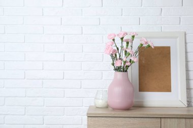 Vazodaki karanfil çiçekleri ve beyaz tuğla duvarın yanındaki ahşap dolaptaki diğer dekorlar.