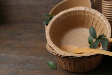 Set of disposable tableware and green leaves on wooden table, closeup. Space for text