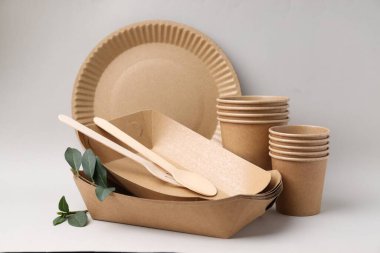 Açık gri arkaplanda tek kullanımlık sofra takımı ve yeşil yapraklar