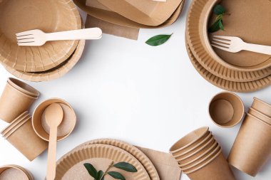 Set of disposable tableware and green leaves on white background, flat lay. Space for text