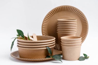 Beyaz arkaplanda tek kullanımlık eşyalar ve yeşil yapraklar, yakın plan